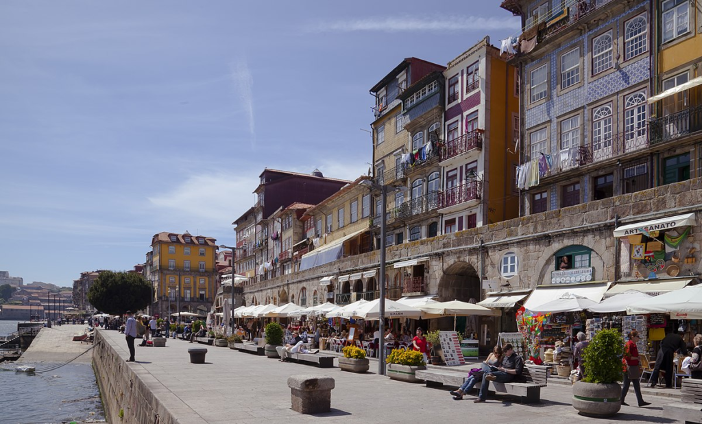 The lively scene at Cais da Ribeira, Porto, has colorful traditional buildings and bustling waterfront cafes along the Douro River.