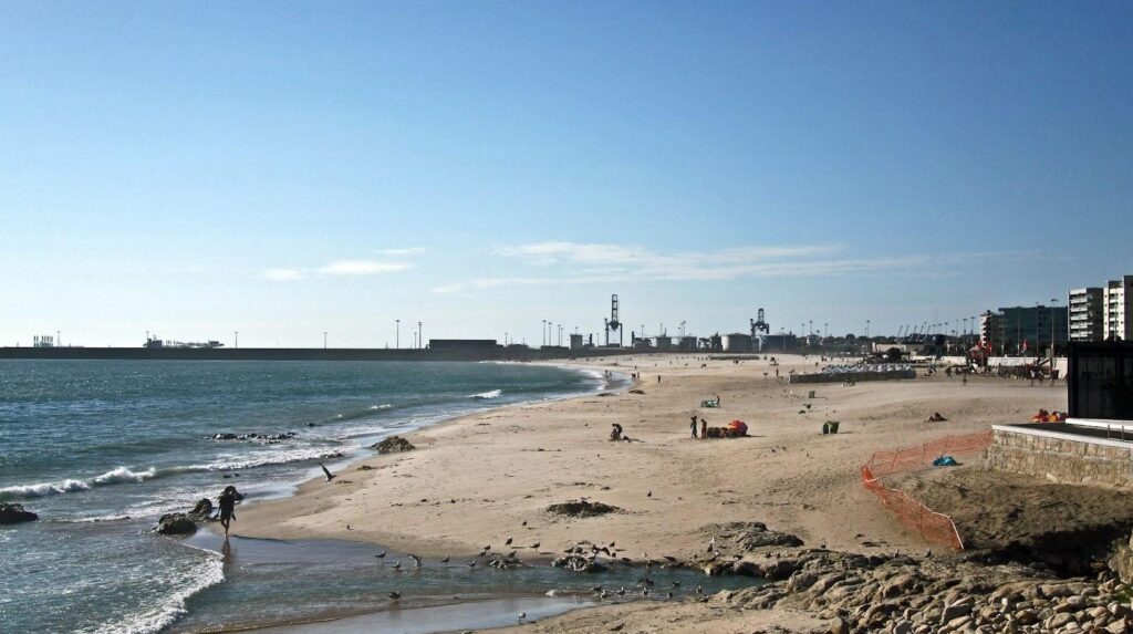 Wide, sandy shores of Matosinhos Beach near Porto, with waves gently breaking and a lively crowd enjoying the coastal scenery.